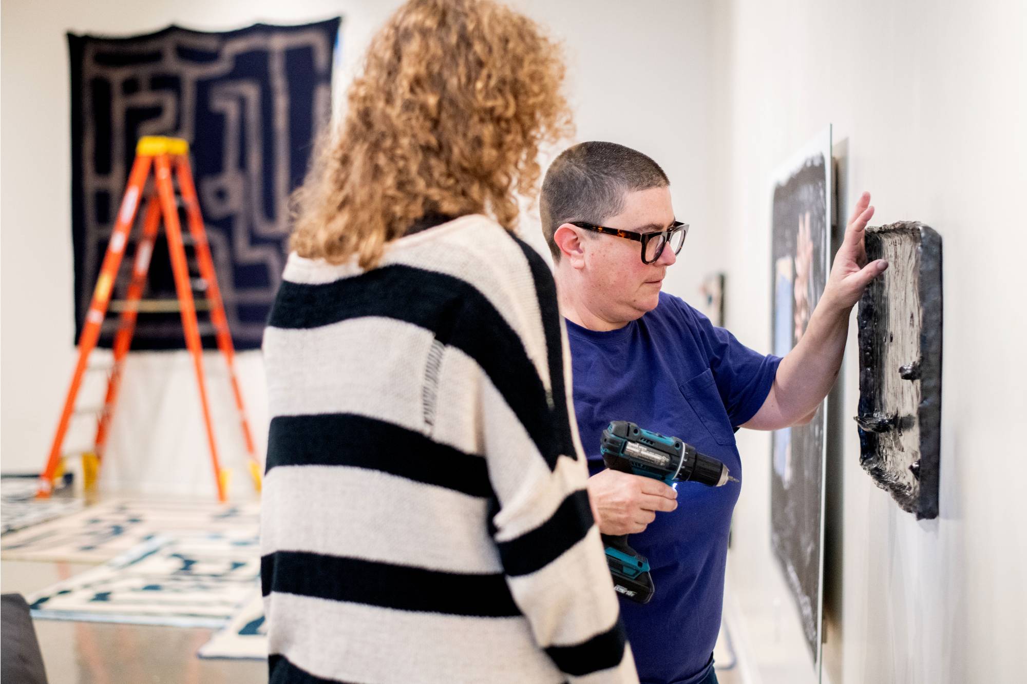 Students working to hang an image-based ceramic artwork with guest artist Emmy Bright.